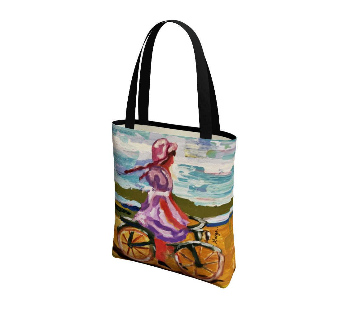 A canvas tote bag with black handles, featuring a colorful artistic print of a woman riding a bicycle by the sea. The print has a textured, impressionistic style with blue, pink, orange, and green tones.