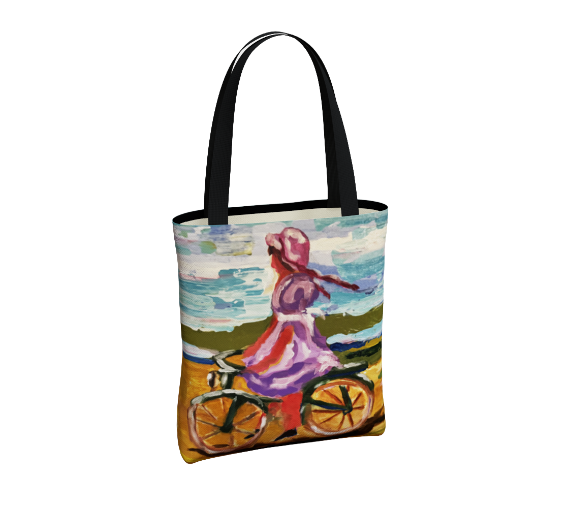 A tote bag with black handles and a colorful printed illustration of a woman riding a bicycle by the sea, shown on a plain white background.