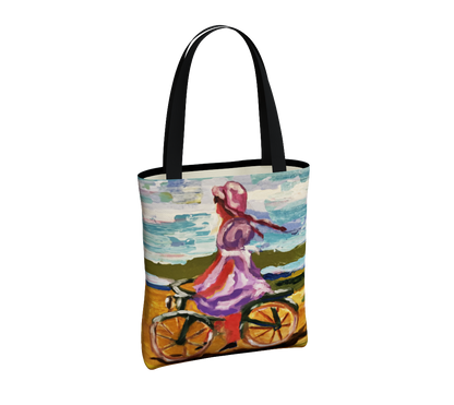 A tote bag with black handles and a colorful printed illustration of a woman riding a bicycle by the sea, shown on a plain white background.