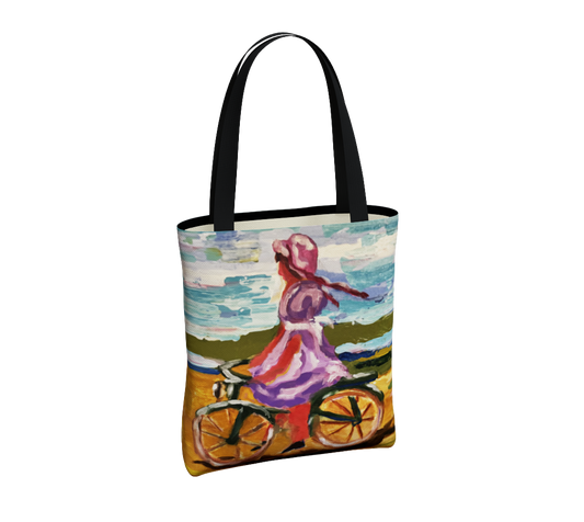 A tote bag with black handles and a colorful printed illustration of a woman riding a bicycle by the sea, shown on a plain white background.